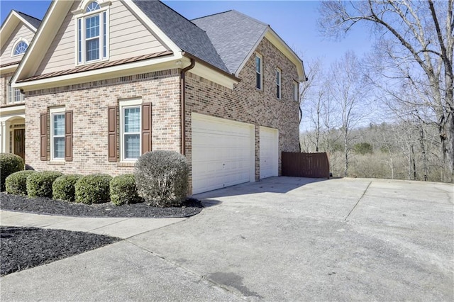 view of property exterior with brick siding, driveway, roof with shingles, and fence