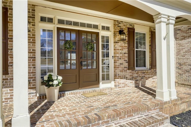 doorway to property featuring french doors, brick siding, and a porch