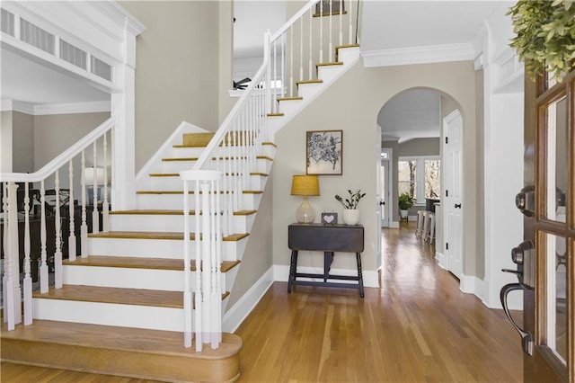 stairway featuring wood finished floors, baseboards, arched walkways, ornamental molding, and a towering ceiling