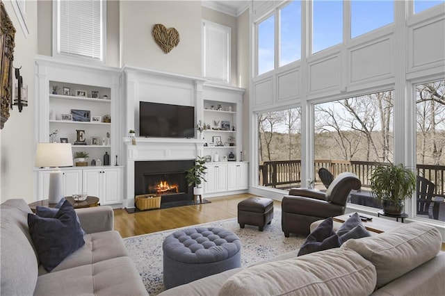 living room with a fireplace with flush hearth, built in shelves, a high ceiling, and wood finished floors