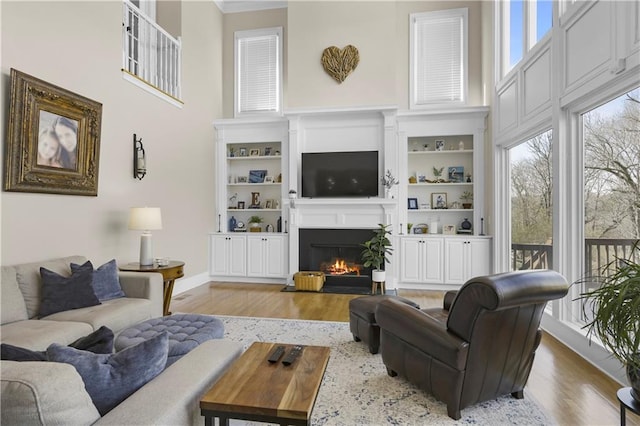 living room with wood finished floors, a healthy amount of sunlight, a towering ceiling, and a warm lit fireplace