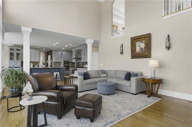 living room featuring a high ceiling, light wood-style flooring, baseboards, and ornate columns