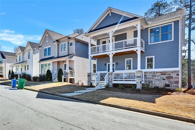 view of front of house with a balcony, covered porch, a residential view, and stone siding