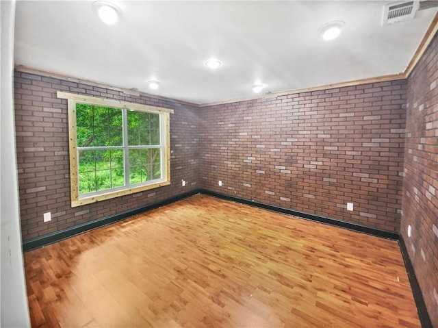 empty room featuring hardwood / wood-style floors, ornamental molding, and brick wall