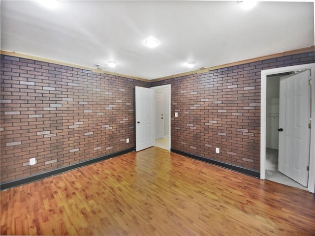 spare room with light wood-type flooring and brick wall