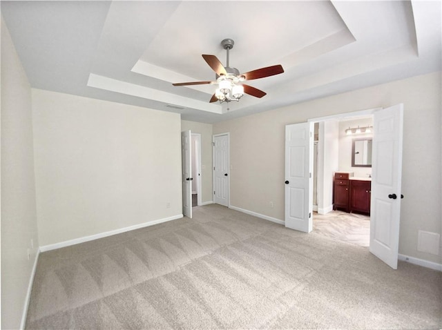 unfurnished bedroom with light carpet, a tray ceiling, ensuite bath, and ceiling fan