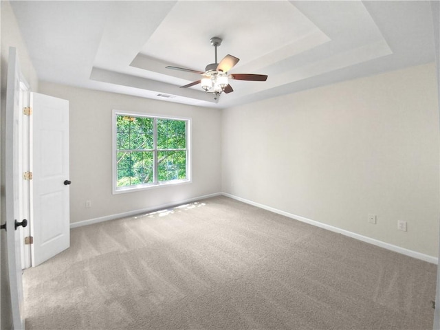 empty room featuring ceiling fan, a raised ceiling, and light colored carpet