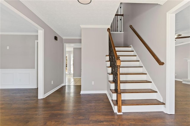 stairway with ornamental molding, wood finished floors, a wainscoted wall, and a textured ceiling