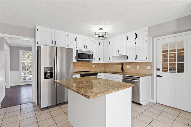 kitchen featuring light stone counters, light tile patterned flooring, a sink, stainless steel appliances, and white cabinets