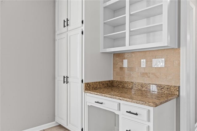 kitchen featuring stone countertops, open shelves, backsplash, white cabinetry, and baseboards