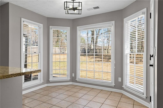 unfurnished dining area featuring light tile patterned flooring, visible vents, a textured ceiling, and baseboards