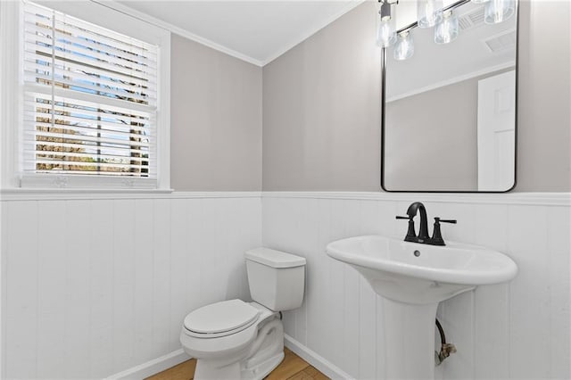 half bath with a wainscoted wall, toilet, crown molding, and wood finished floors