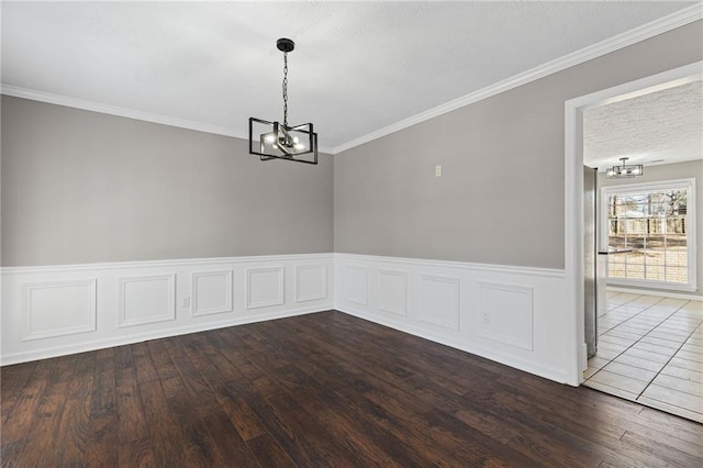 empty room featuring a wainscoted wall, crown molding, an inviting chandelier, and wood finished floors