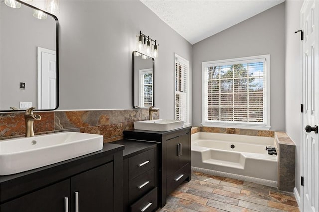 full bath with vanity, vaulted ceiling, a garden tub, and a textured ceiling