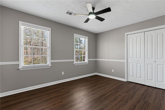 unfurnished bedroom with a closet, baseboards, a textured ceiling, and dark wood-style flooring