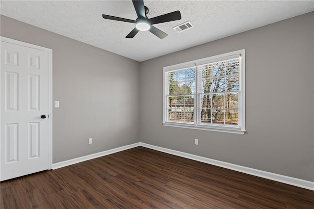 empty room featuring dark wood finished floors, visible vents, a textured ceiling, and baseboards