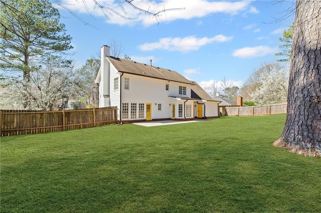 rear view of house featuring a patio area, a lawn, a chimney, and a fenced backyard