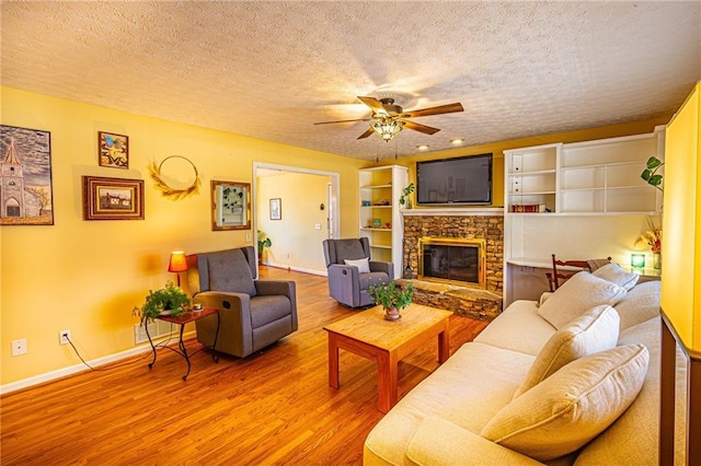 living room with hardwood / wood-style flooring, ceiling fan, a stone fireplace, and a textured ceiling