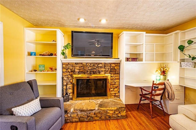 living room with hardwood / wood-style flooring, a stone fireplace, and a textured ceiling