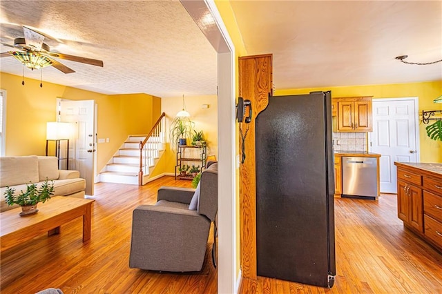 kitchen featuring ceiling fan, black refrigerator, light hardwood / wood-style floors, decorative backsplash, and stainless steel dishwasher