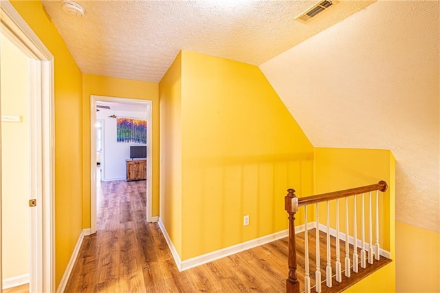 hall with lofted ceiling, hardwood / wood-style floors, and a textured ceiling