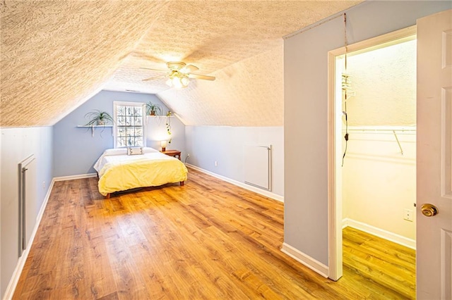 unfurnished bedroom featuring ceiling fan, vaulted ceiling, hardwood / wood-style floors, a textured ceiling, and a walk in closet