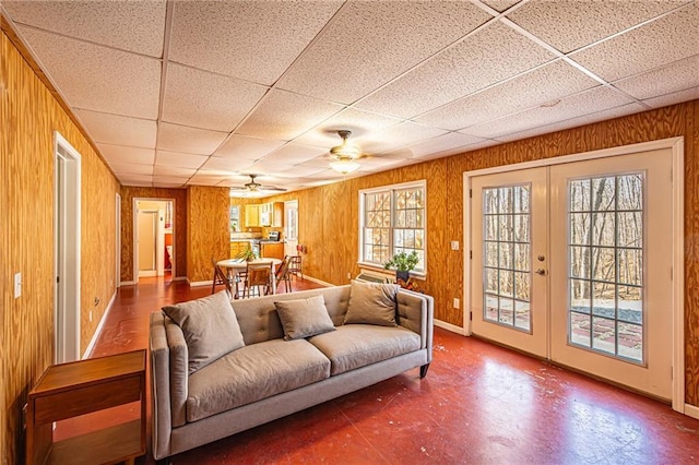 living room featuring a drop ceiling, french doors, and wood walls