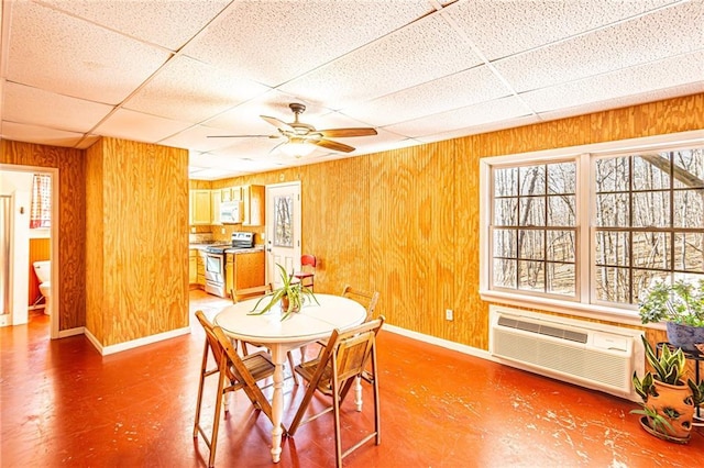 dining area featuring a drop ceiling, wooden walls, an AC wall unit, and ceiling fan