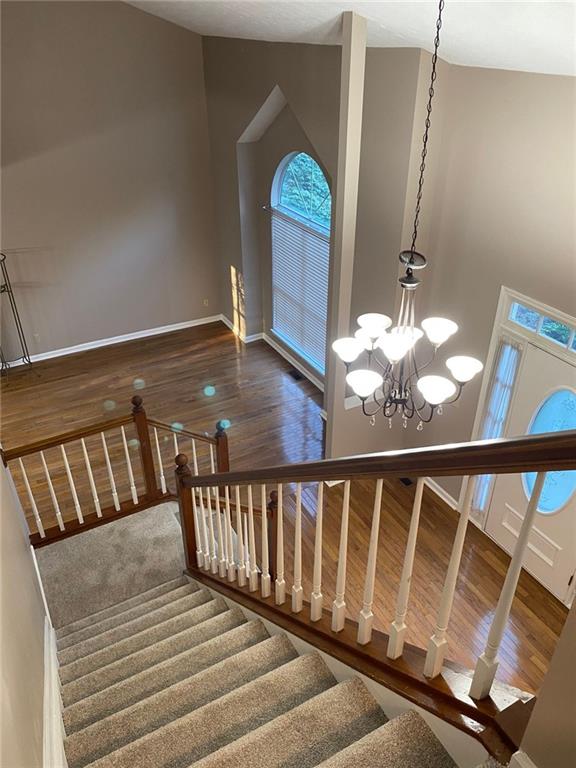 stairs with hardwood / wood-style flooring, a healthy amount of sunlight, high vaulted ceiling, and a notable chandelier