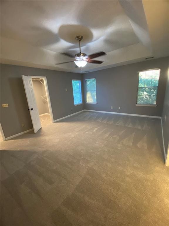 unfurnished bedroom featuring multiple windows, ceiling fan, carpet, and a walk in closet