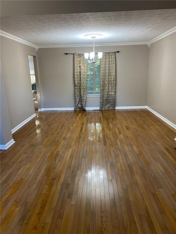 unfurnished dining area featuring an inviting chandelier, crown molding, and dark wood-type flooring