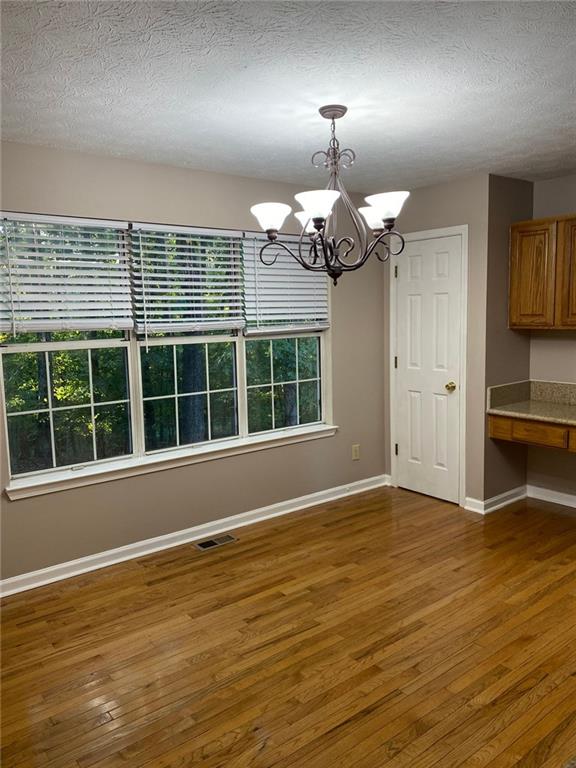 unfurnished dining area featuring a notable chandelier, a textured ceiling, a wealth of natural light, and dark hardwood / wood-style flooring