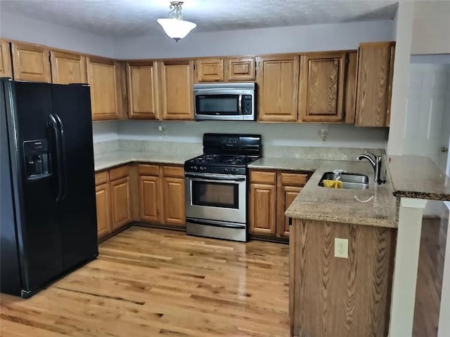 kitchen with appliances with stainless steel finishes, sink, kitchen peninsula, light hardwood / wood-style floors, and light stone counters