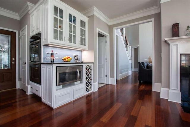 kitchen featuring dark wood-type flooring, tasteful backsplash, stainless steel microwave, and white cabinets