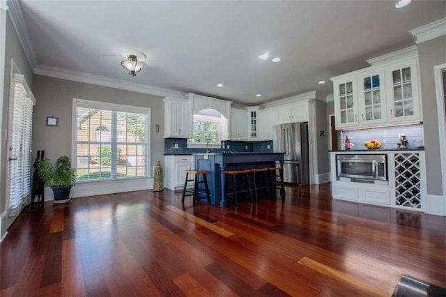 kitchen with white cabinets, dark hardwood / wood-style floors, appliances with stainless steel finishes, decorative backsplash, and a kitchen bar