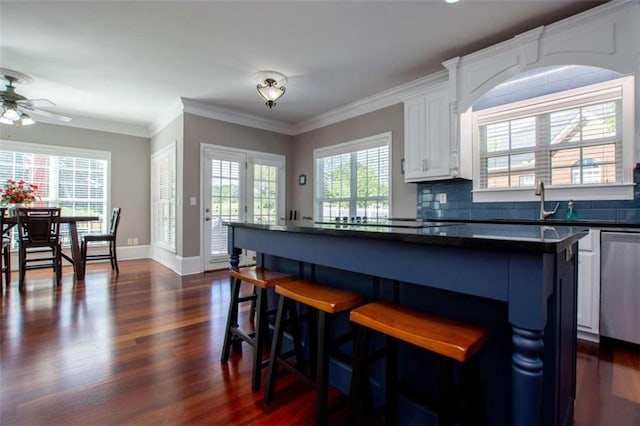 kitchen featuring white cabinets, backsplash, dark wood-type flooring, ceiling fan, and ornamental molding