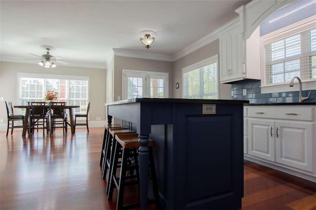 kitchen with white cabinetry, dark hardwood / wood-style flooring, crown molding, a kitchen bar, and backsplash