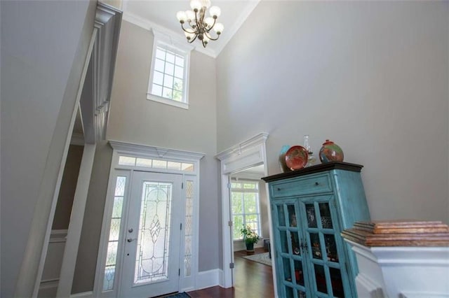 entryway with a notable chandelier, hardwood / wood-style flooring, high vaulted ceiling, and crown molding