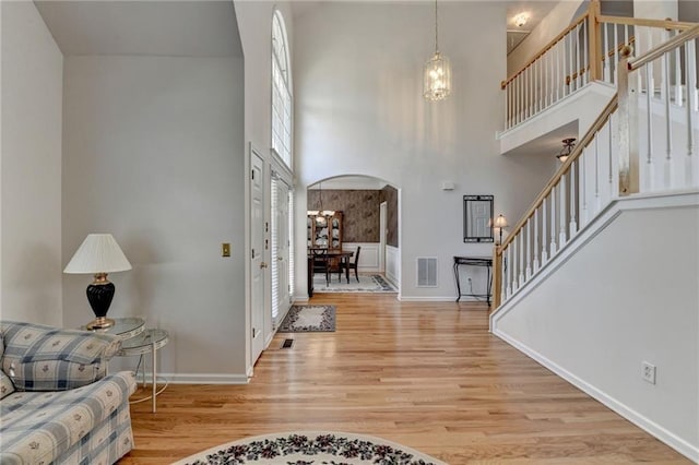 foyer with visible vents, stairway, a towering ceiling, wood finished floors, and arched walkways