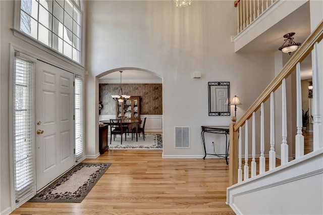 entryway featuring light wood-style floors, arched walkways, visible vents, and a towering ceiling