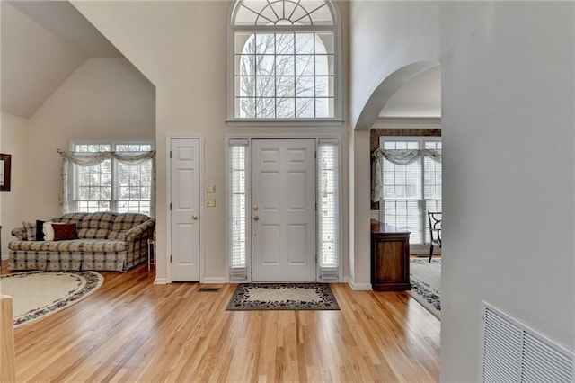 entryway featuring arched walkways, visible vents, high vaulted ceiling, and wood finished floors