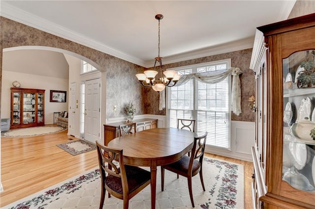 dining room with wallpapered walls, arched walkways, a chandelier, and wainscoting