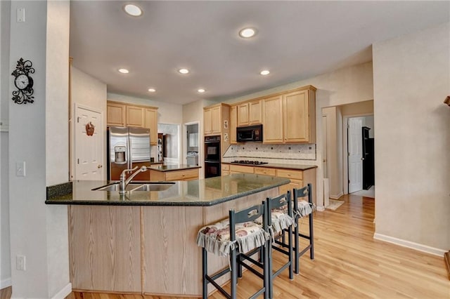 kitchen featuring light brown cabinetry, a breakfast bar, light wood-style flooring, black appliances, and a sink