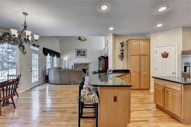 kitchen featuring light brown cabinets, a peninsula, a sink, a stone fireplace, and dark countertops