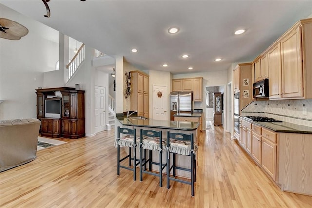 kitchen featuring a kitchen bar, black appliances, light wood-style flooring, light brown cabinetry, and dark countertops