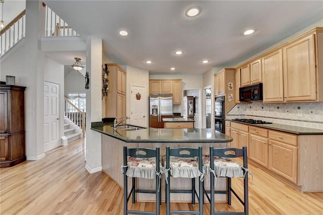 kitchen featuring light brown cabinetry, black appliances, dark countertops, and a sink