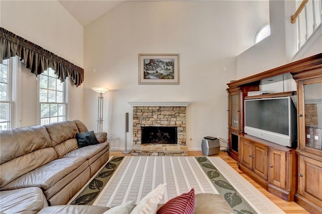 living area featuring a stone fireplace, baseboard heating, high vaulted ceiling, and light wood-style floors