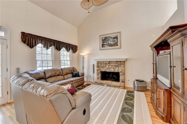 living area with high vaulted ceiling, light wood-style flooring, a fireplace, baseboards, and ceiling fan