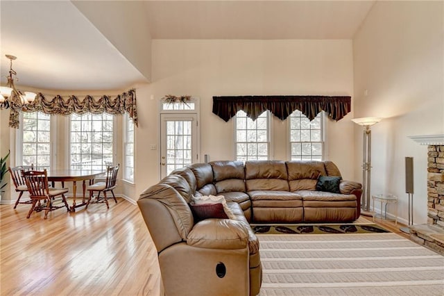 living area featuring baseboards, light wood-type flooring, an inviting chandelier, and a towering ceiling