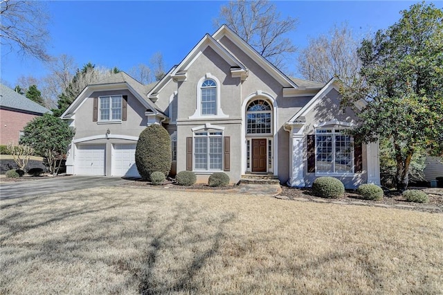 traditional home with a front lawn, an attached garage, aphalt driveway, and stucco siding